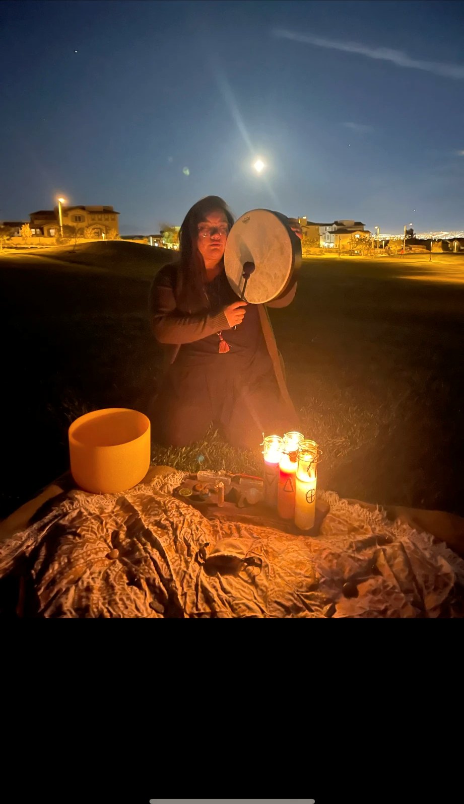 Xsana Saphire drumming beside candlelight under a full moon