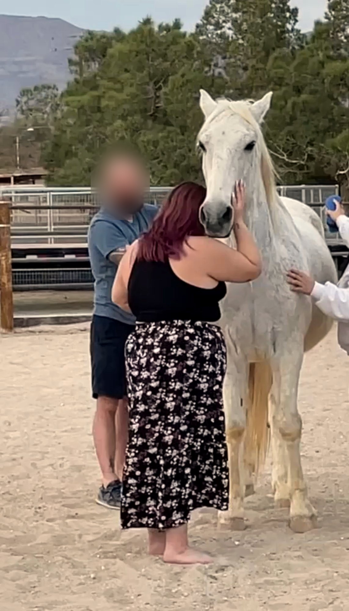 Xsana Saphire resting her head against a white horse during an equine-facilitated session at a Las Vegas barn