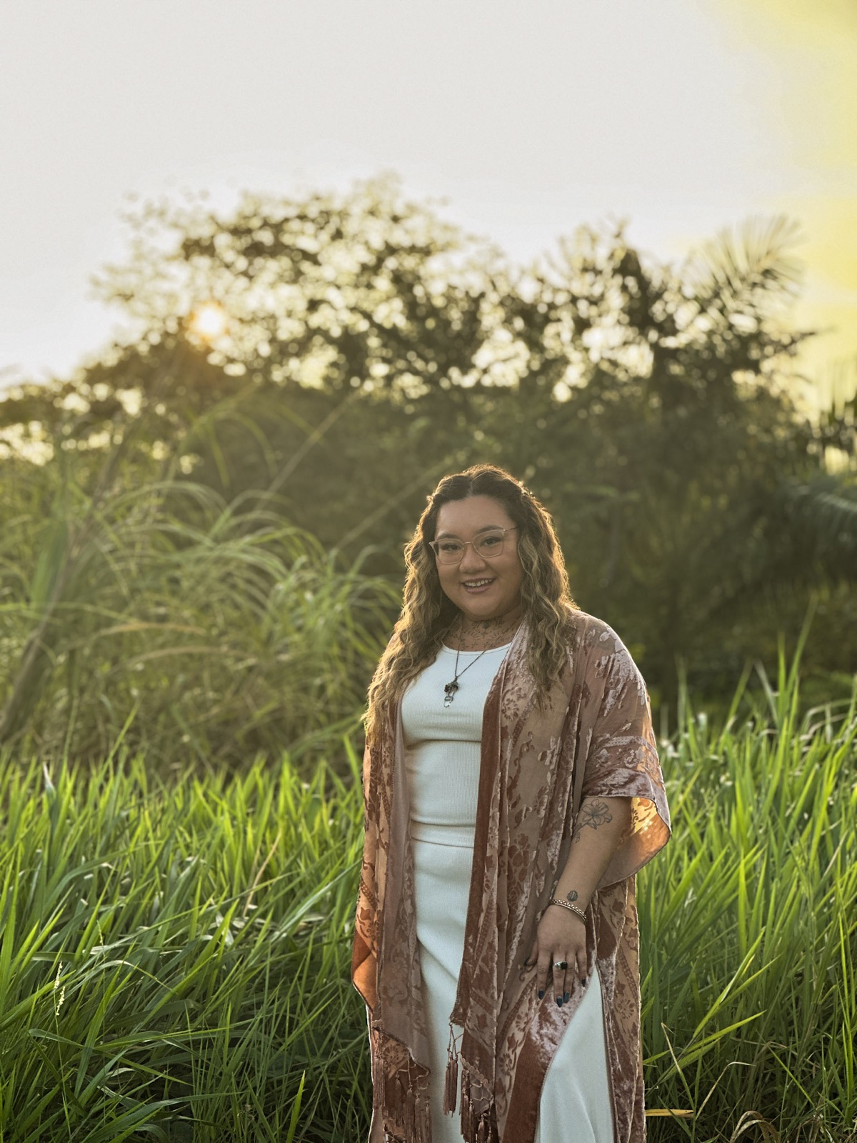 Xsana Saphire, LCPC — standing in golden-hour tall grass, a warm, open three-quarter expression