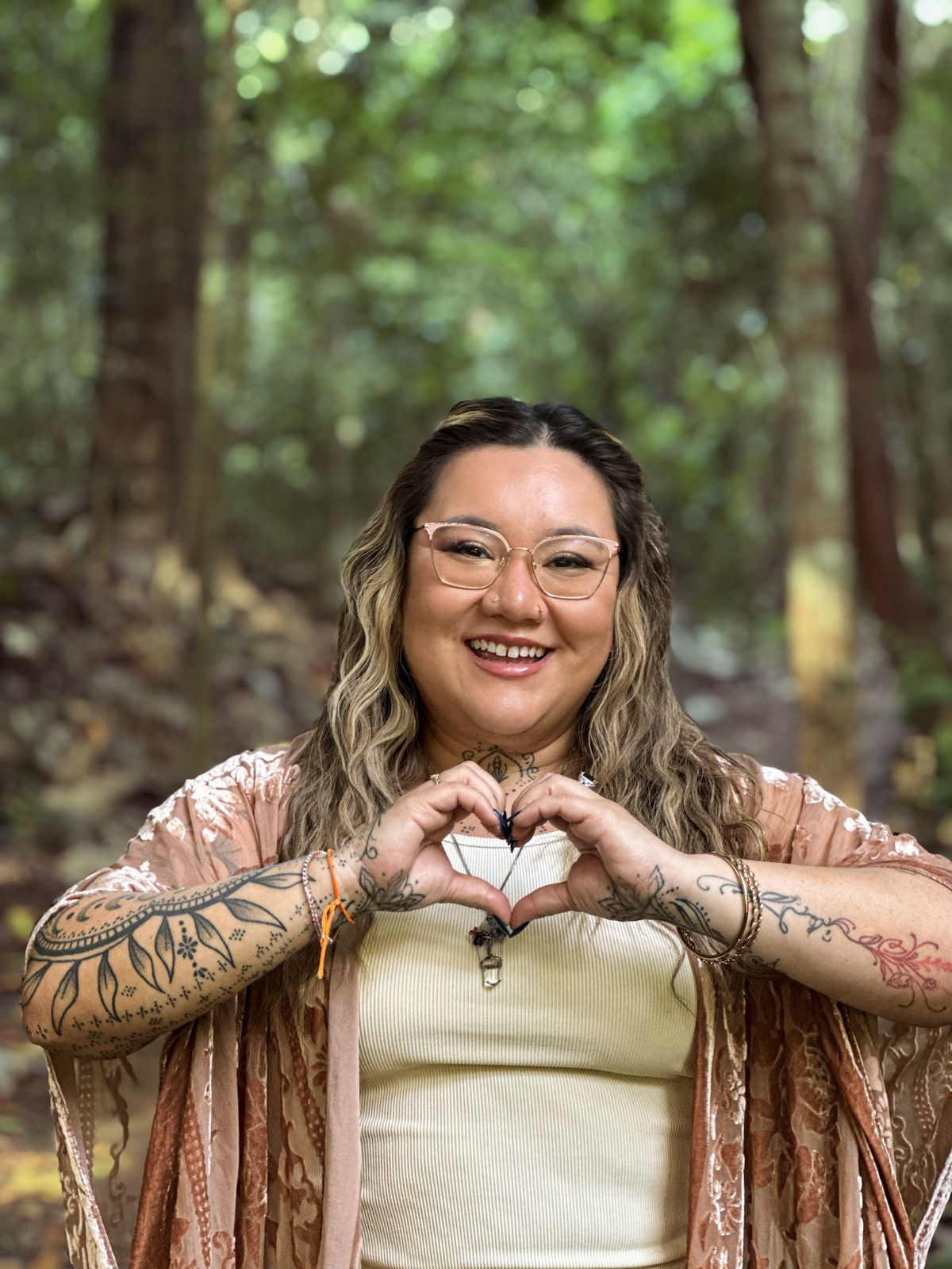 Xsana Saphire smiling in soft forest light, her hands forming a heart