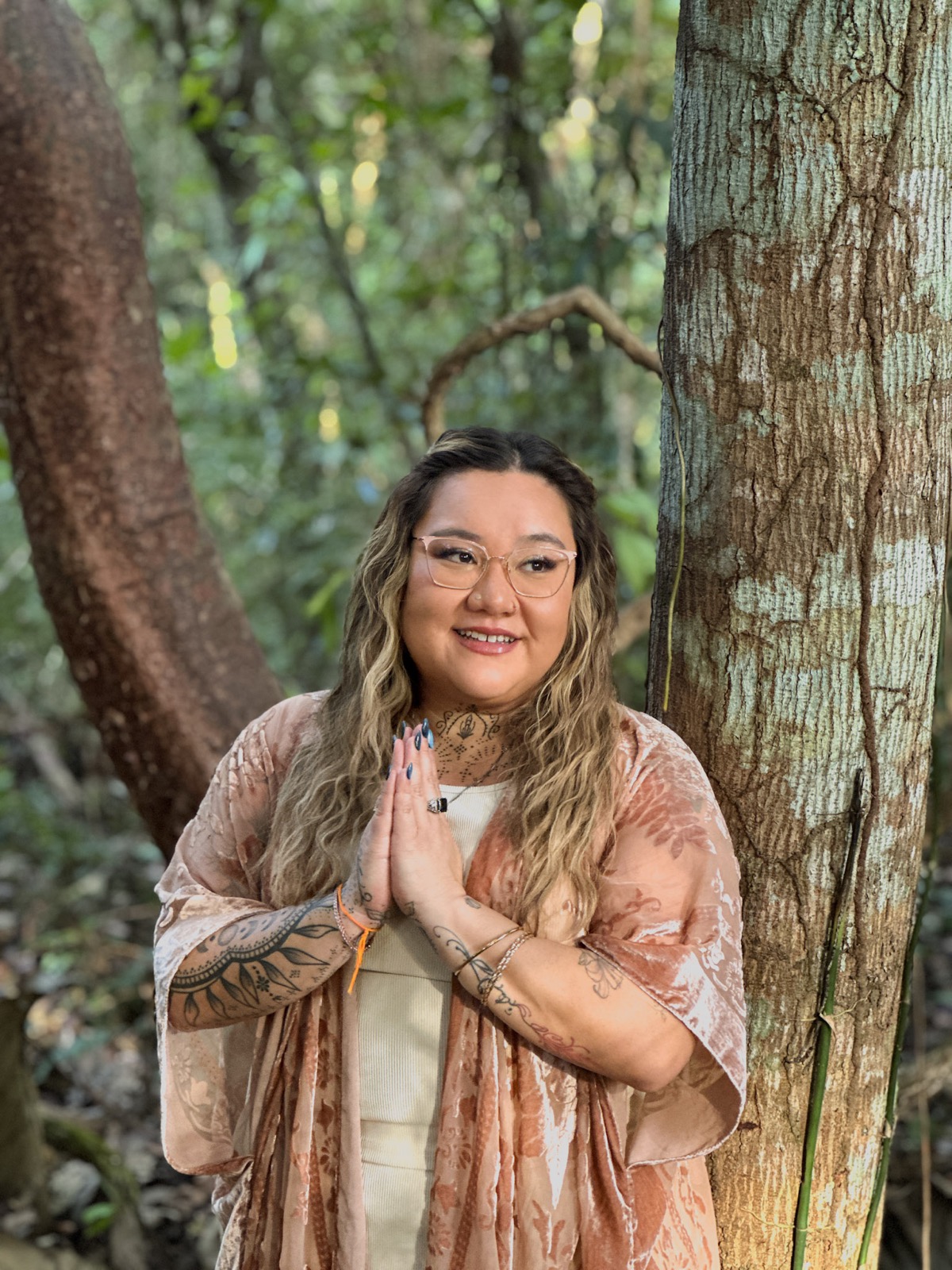 Xsana Saphire standing in golden light beneath a wide branching tree — open, grounded, fully present